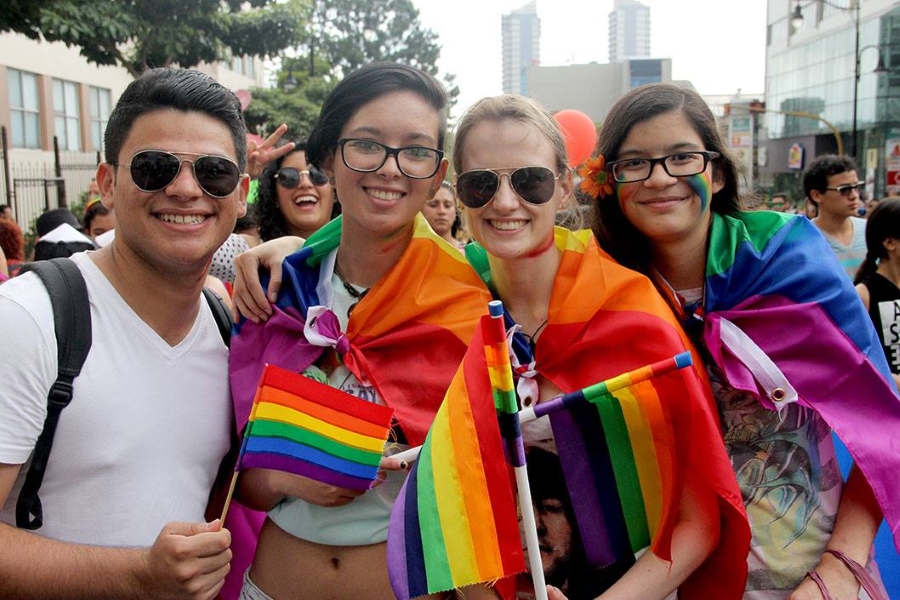 Grupo de 4 personas portando bandera multicolor símbolo de la Diversidad